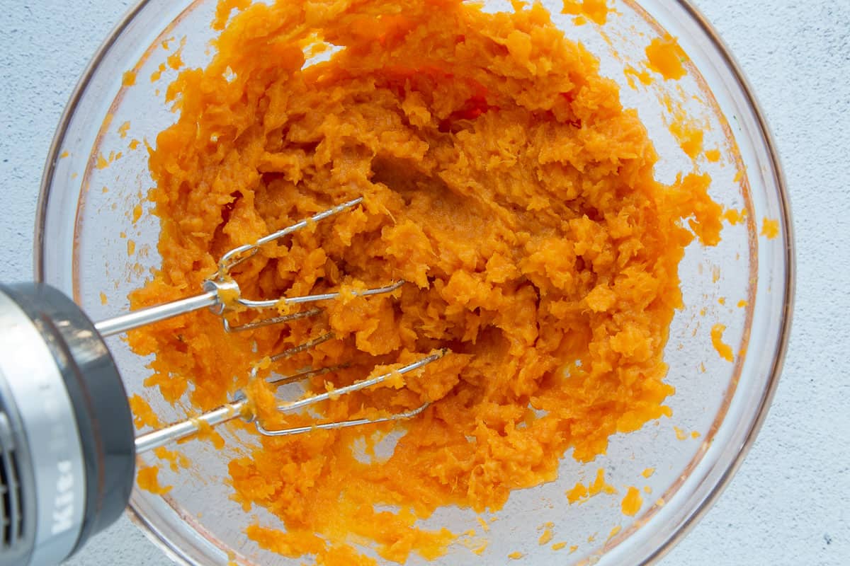 mashed sweet potatoes in a glass bowl with a hand mixer.