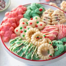 assortment of white, red, and green spritz cookies on a white cake stand with a red rim.