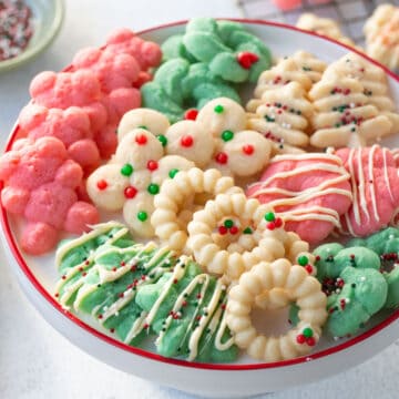 assortment of white, red, and green spritz cookies on a white cake stand with a red rim.