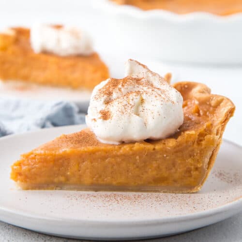 slice of sweet potato pie topped with whipped cream and cinnamon on a white plate.