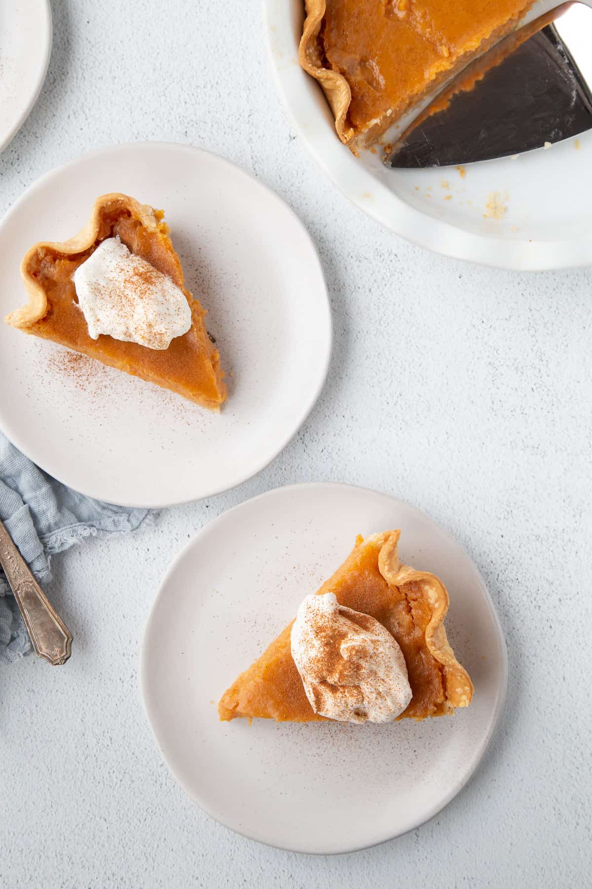 two slices of sweet potato pie topped with whipped cream and cinnamon on two white plates.