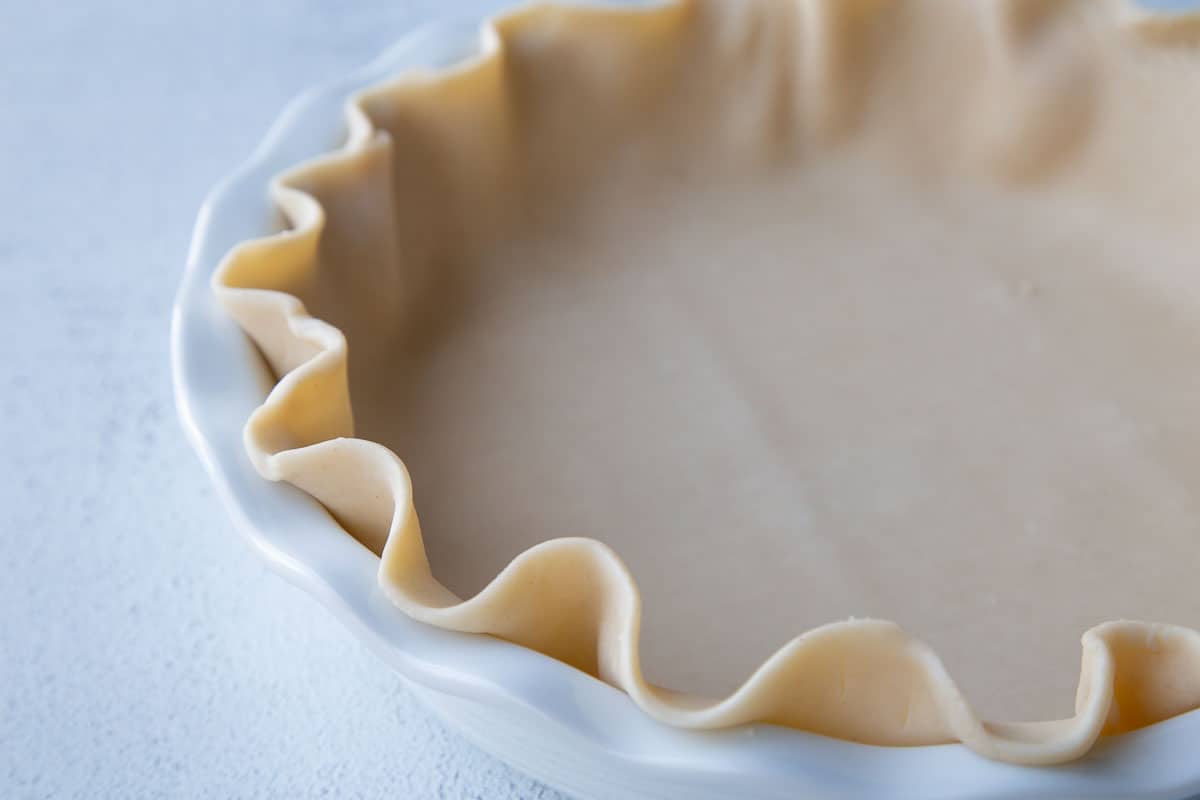 uncooked pie crust with fluted edges in a white pie dish.