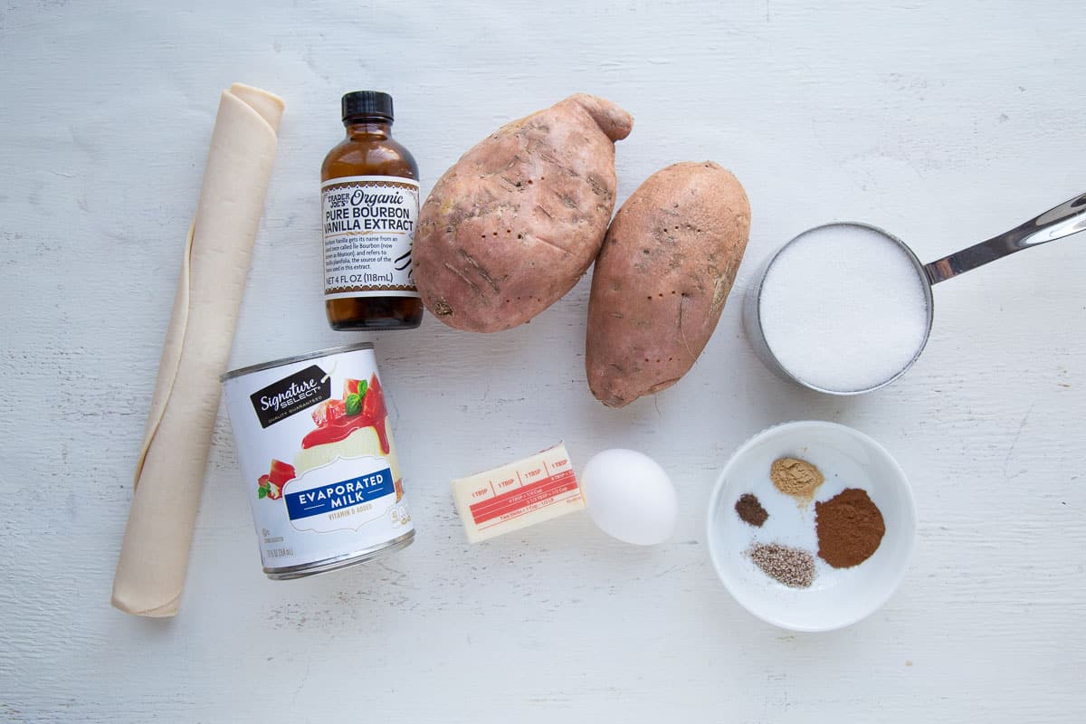 sweet potatoes, pie crust, sugar, and other ingredients on a white table.