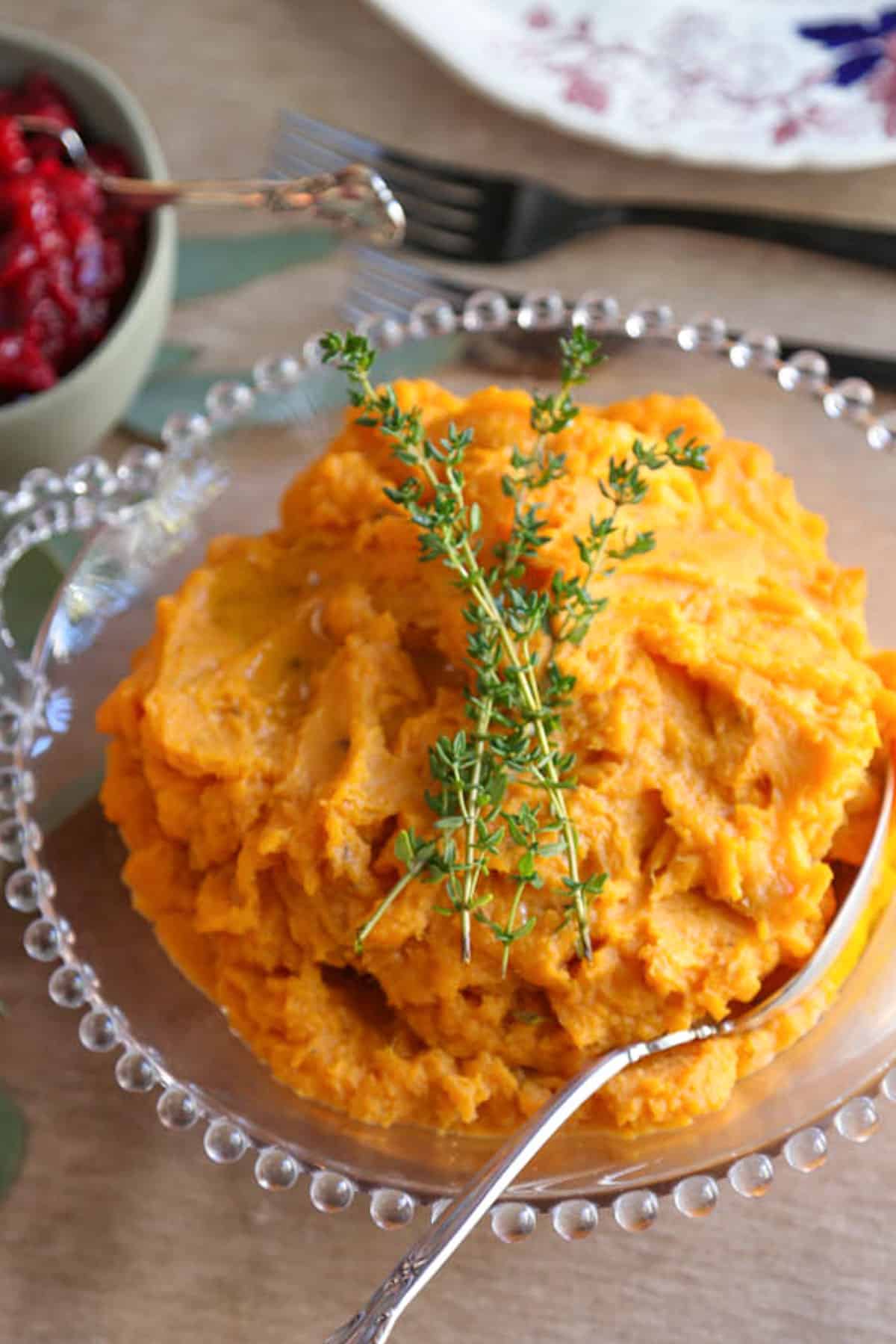 mashed sweet potatoes topped with fresh thyme in a glass decorative dish.