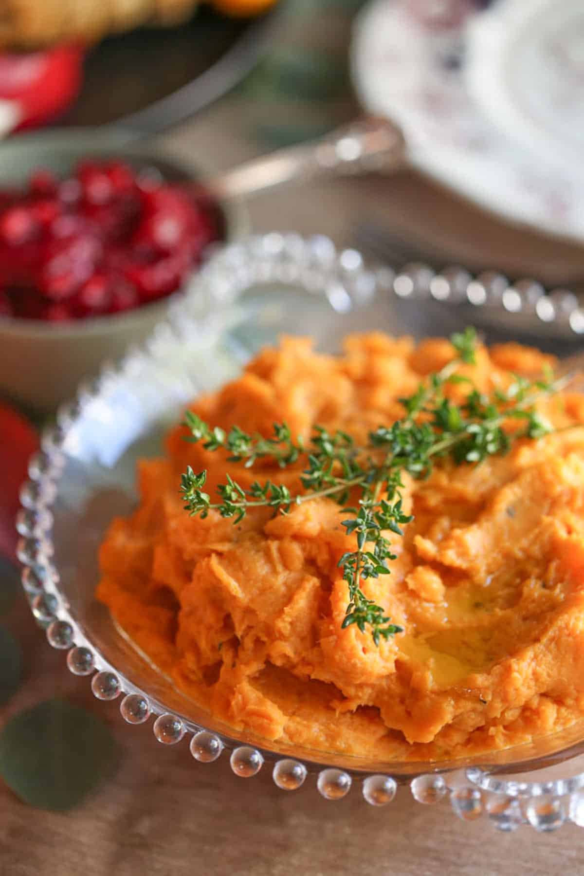 savory mashed sweet potatoes topped with fresh thyme in a decorate glass bowl.