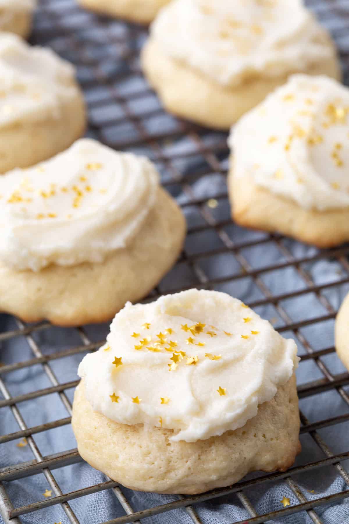 sour cream cookies topped with frosting and gold star sprinkles on a wire rack. 