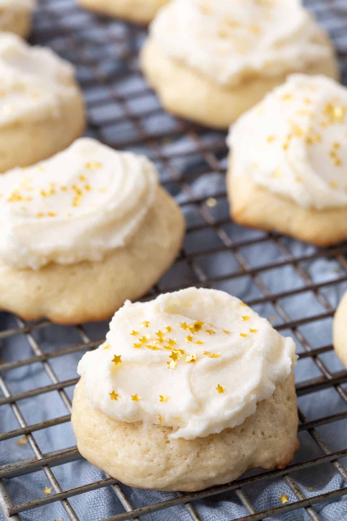 sour cream cookies topped with frosting and gold star sprinkles on a wire rack.