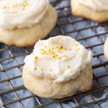 sour cream cookies topped with frosting and gold sprinkles on a wire rack.