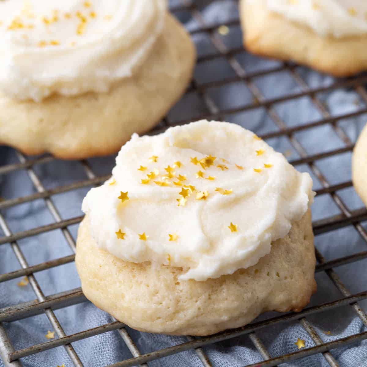 sour cream cookies topped with frosting and gold sprinkles on a wire rack.