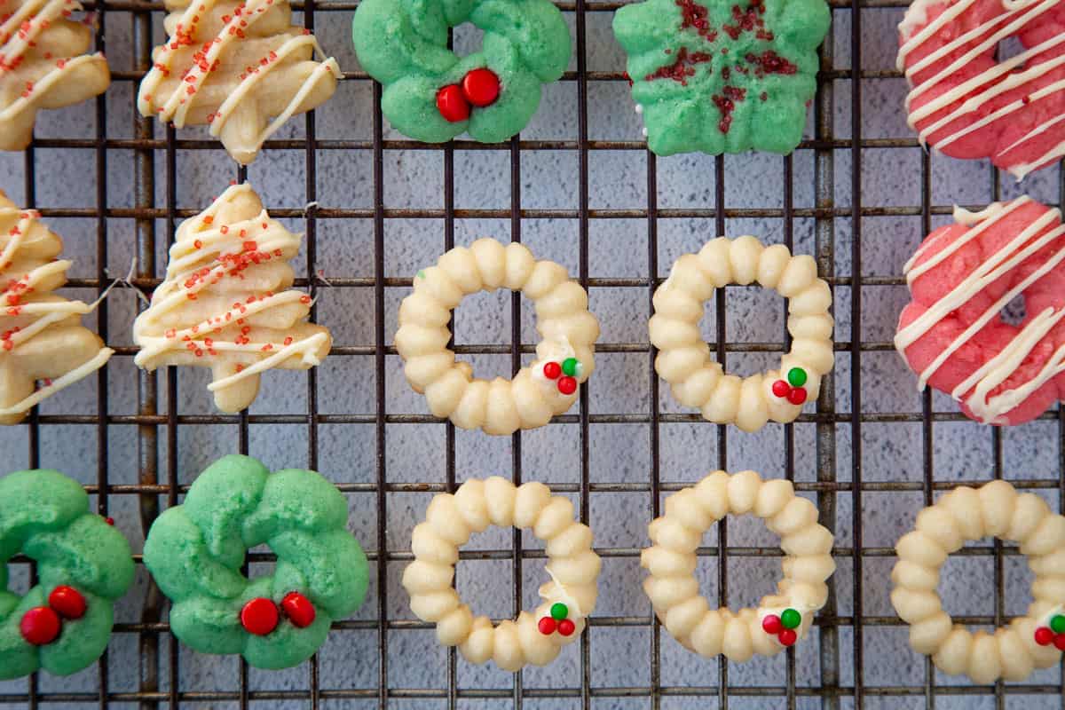 spritz cookies decorated with sprinkles and white chocolate on a wire rack.