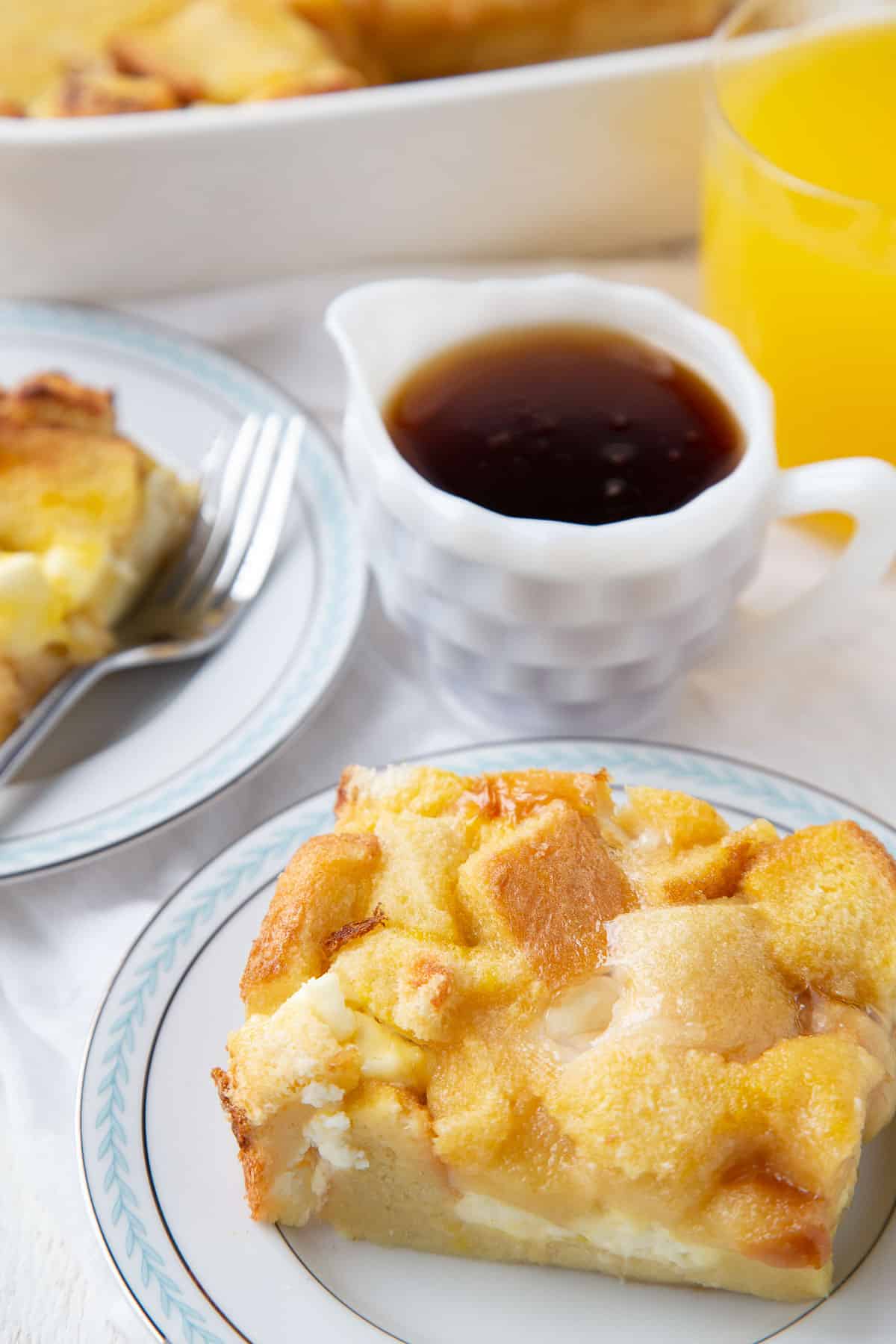 slice of stuffed french toast casserole on a plate next to a mini pitcher of maple syrup.