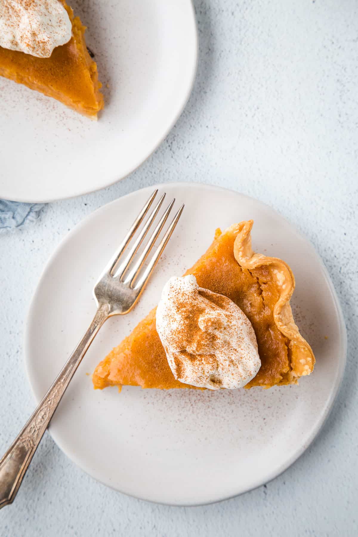 slice of sweet potato pie with a fork on a white plate, topped with whipped cream.