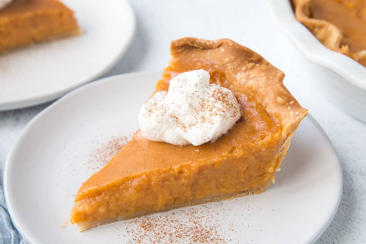 slice of sweet potato pie topped with whipped cream and cinnamon on a white plate.