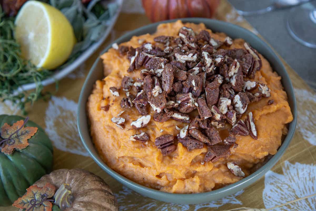 mashed sweet potatoes topped with candied pecans in a green bowl.
