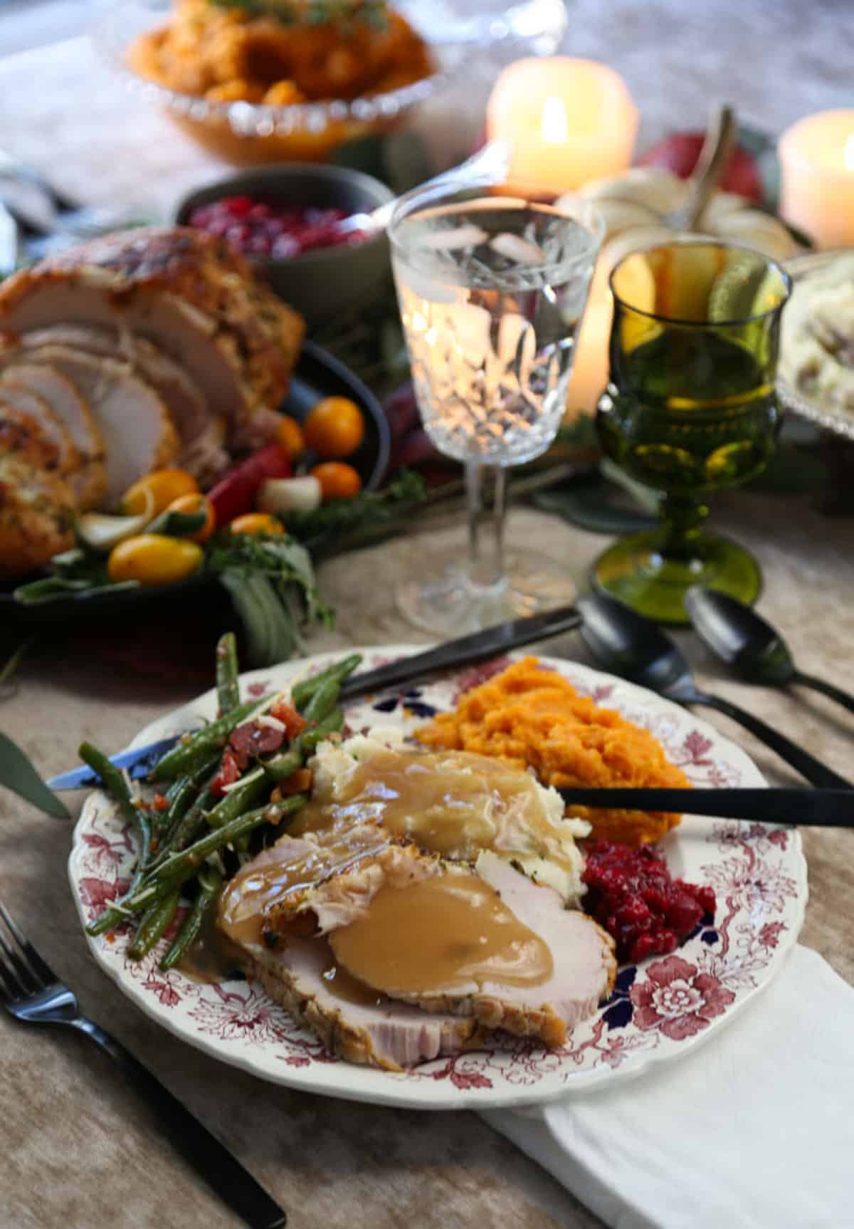 dinner plate filled with turkey slices, green beans, sweet potatoes, and cranberry sauce on a table with candles and mini pumpkins.