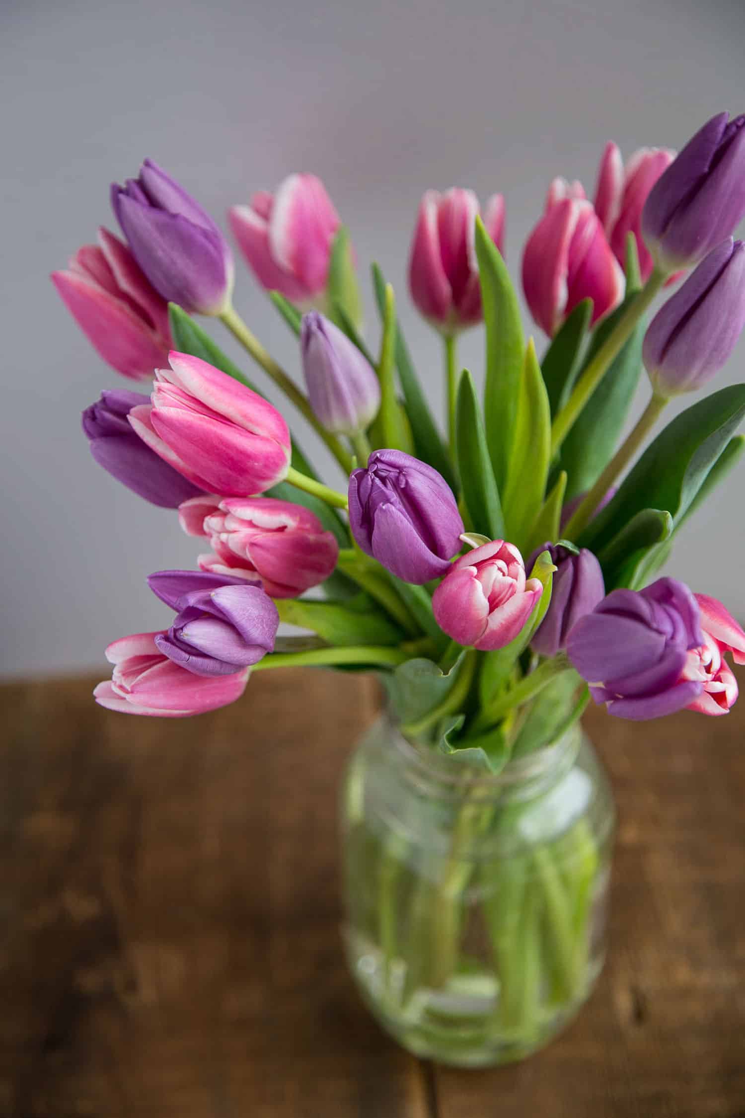 purple and pink tulips in a mason jar on a wooden table.