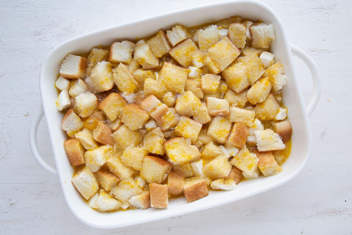 bread cubes soaked with beaten eggs in a white casserole dish.