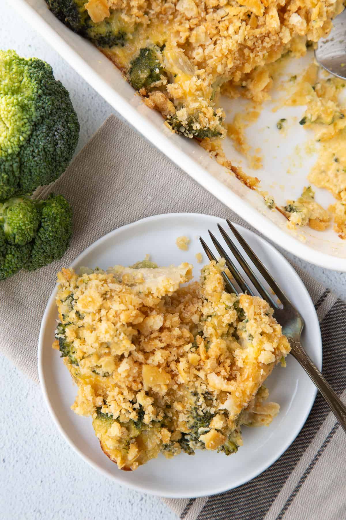 scoop of velveeta broccoli casserole on a small plate with a fork, next to a whole casserole in a white dish.