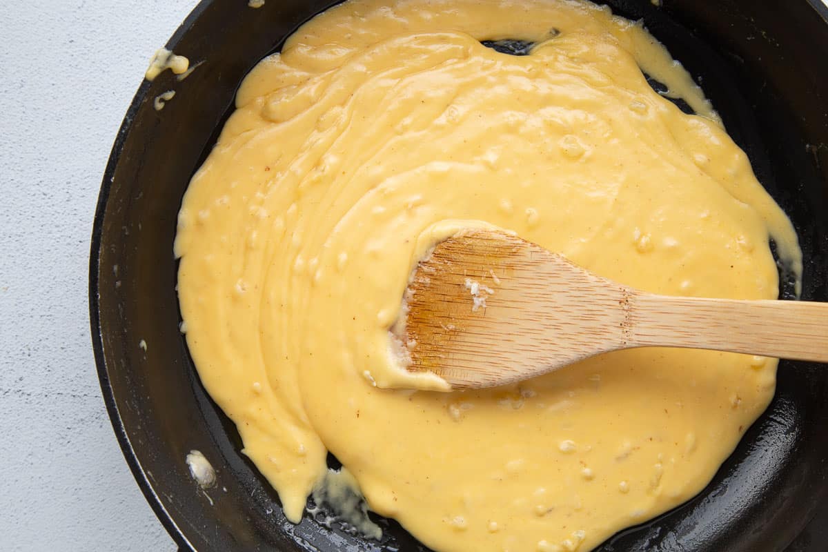 cheese sauce in a skillet with a wooden spoon.