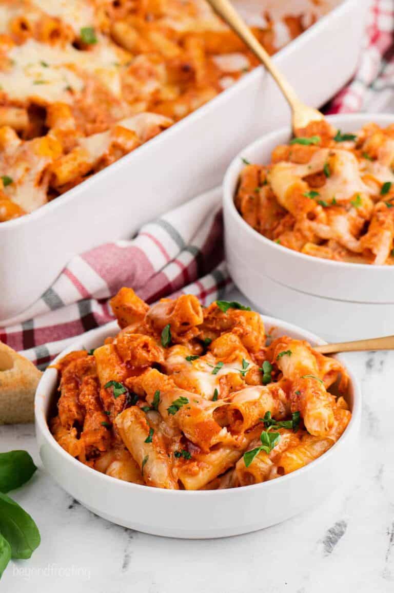 small dish of baked ziti next to a whole casserole dish full of baked ziti.