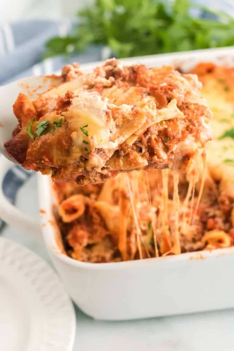 spatula holding a cheesy scoop of gluten free baked ziti above a full casserole dish.