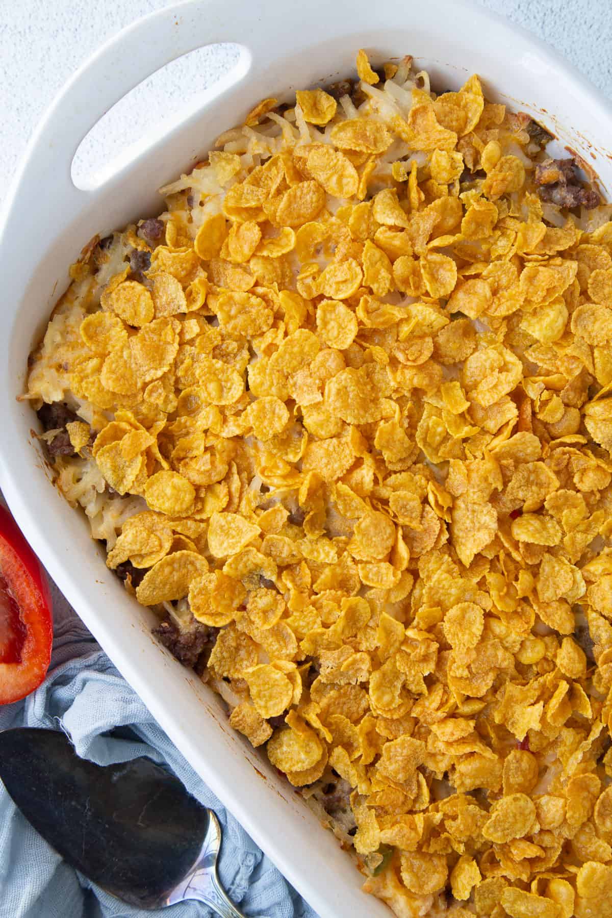 hash brown casserole topped with corn flakes in a white casserole dish.