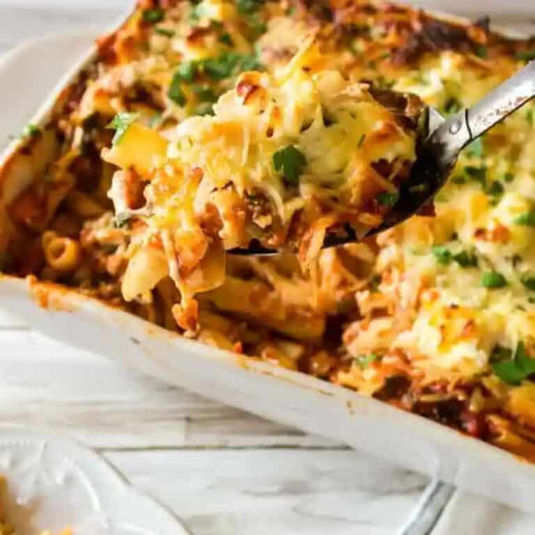 spoon holding a scoop of veggie packed baked ziti above a full casserole dish.