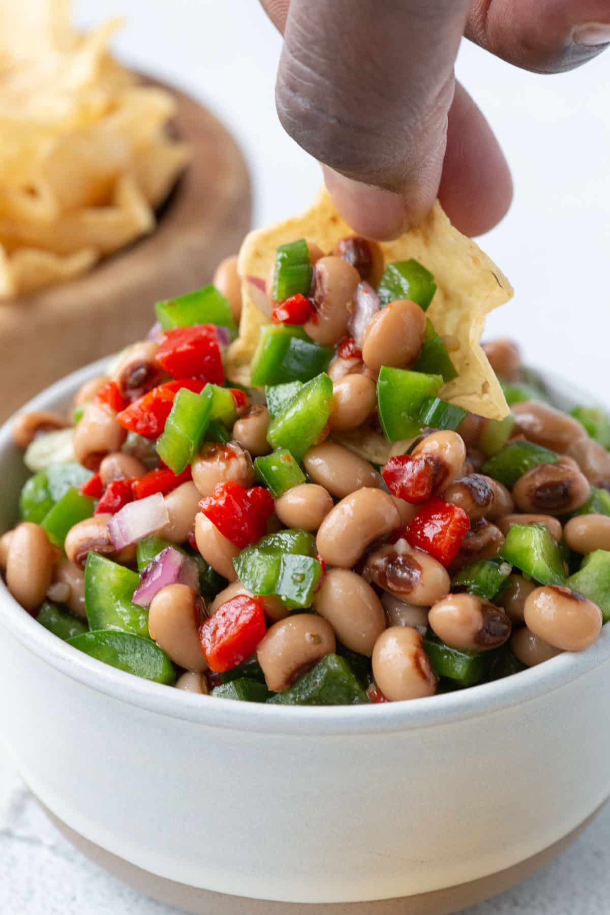 hand dipping a tortilla chip in black eyed pea dip.