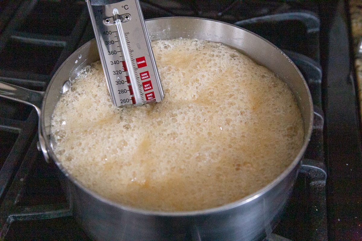 a bubbling sugar mixture in a saucepan with a candy thermometer.