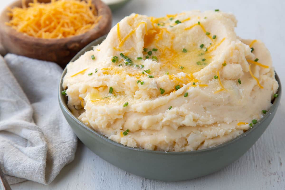 bowl of cheese mashed potatoes with a smaller bowl of shredded cheddar next to it.