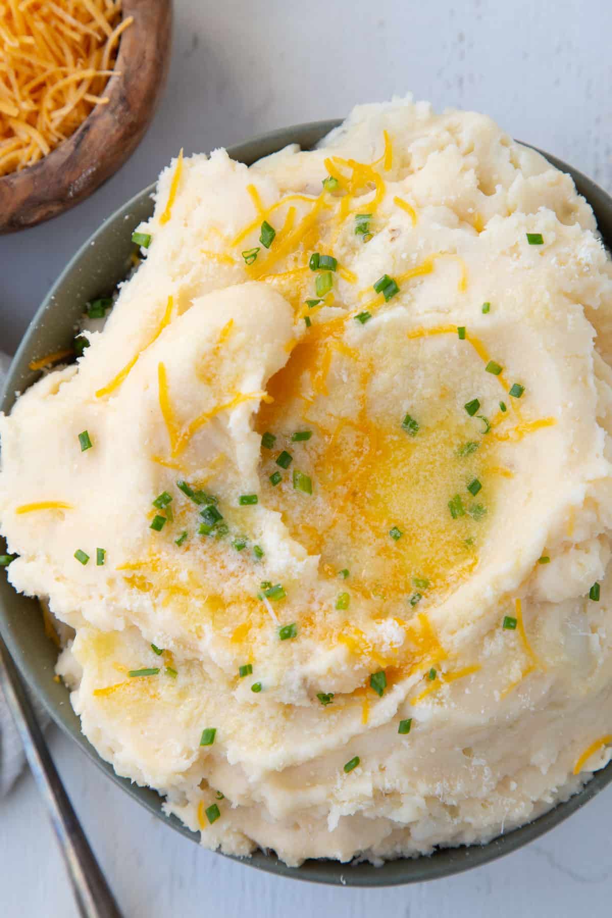 cheesy mashed potatoes in a green bowl, topped with chives and melted butter.