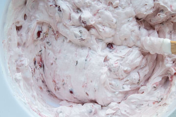 fluffy pink whipped topping mixture with flecks of cherries in a white bowl.