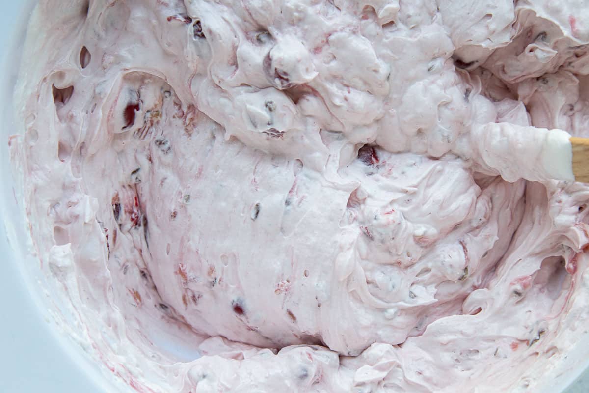 cherry fluff salad in a white bowl with a spatula sticking out.