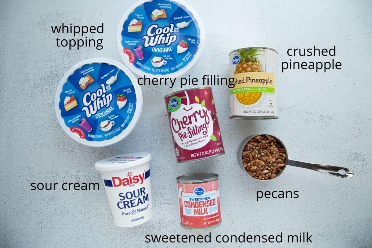 whipped topping, cherry pie filling, sour cream, and other ingredients on a white table.