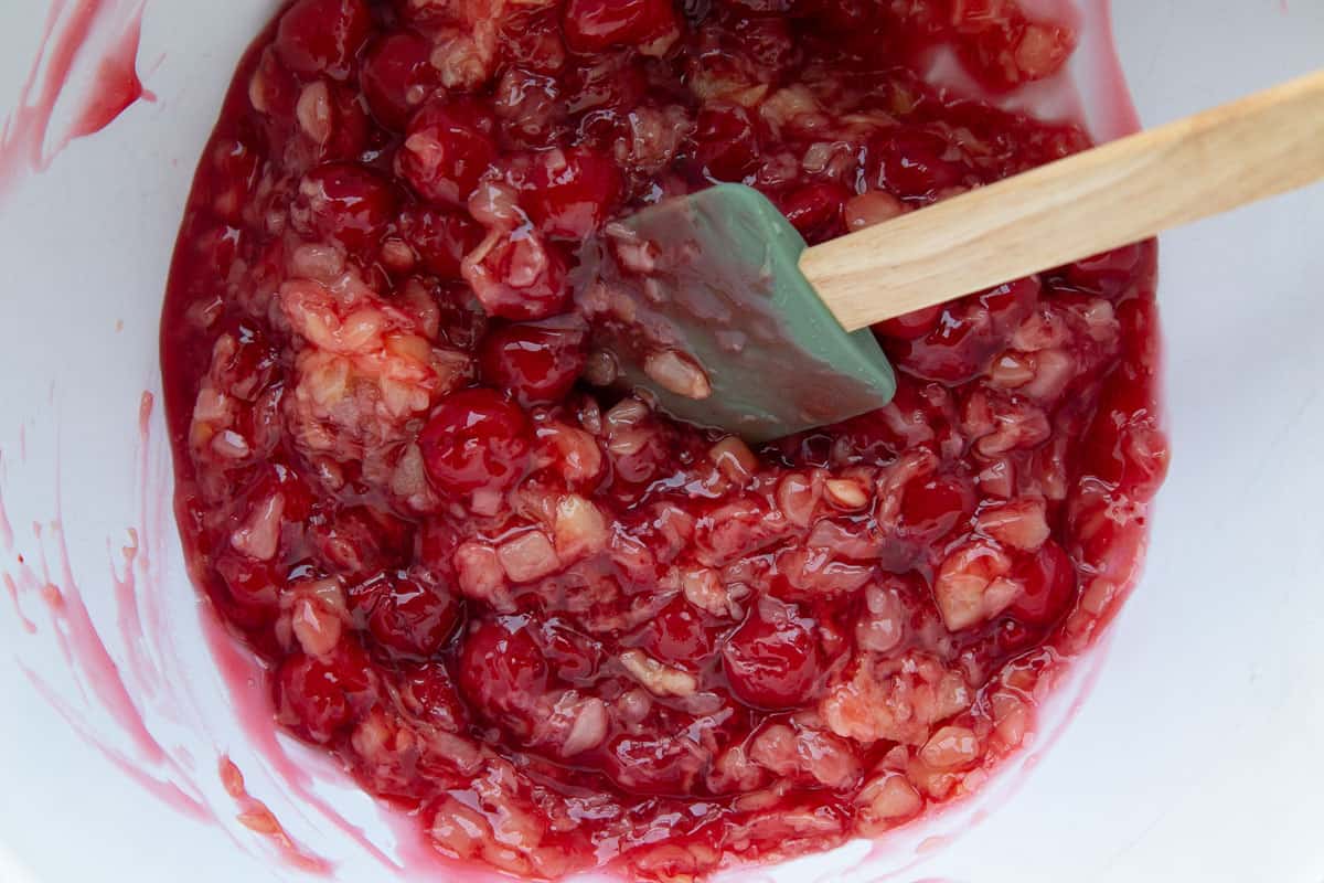 cherry pie filling and crushed pineapple mixed in a white bowl with a spatula.