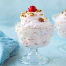 cherry salad topped with a cherry and chopped pecans in a mini glass parfait dish.