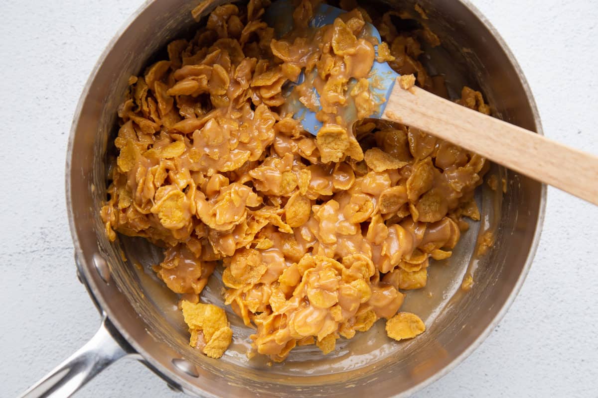 peanut butter corn flake mixture in a saucepan with a spatula.