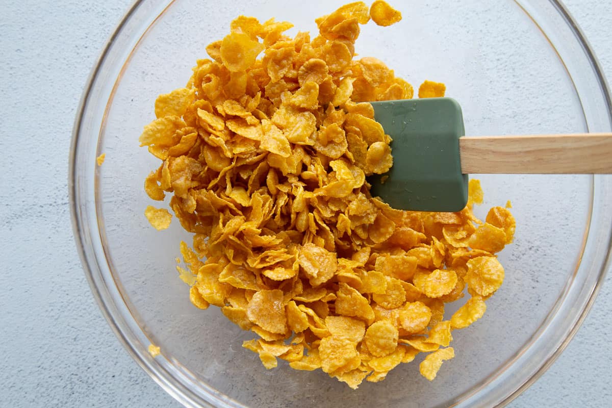 corn flakes and butter in a glass bowl with a green spatula.