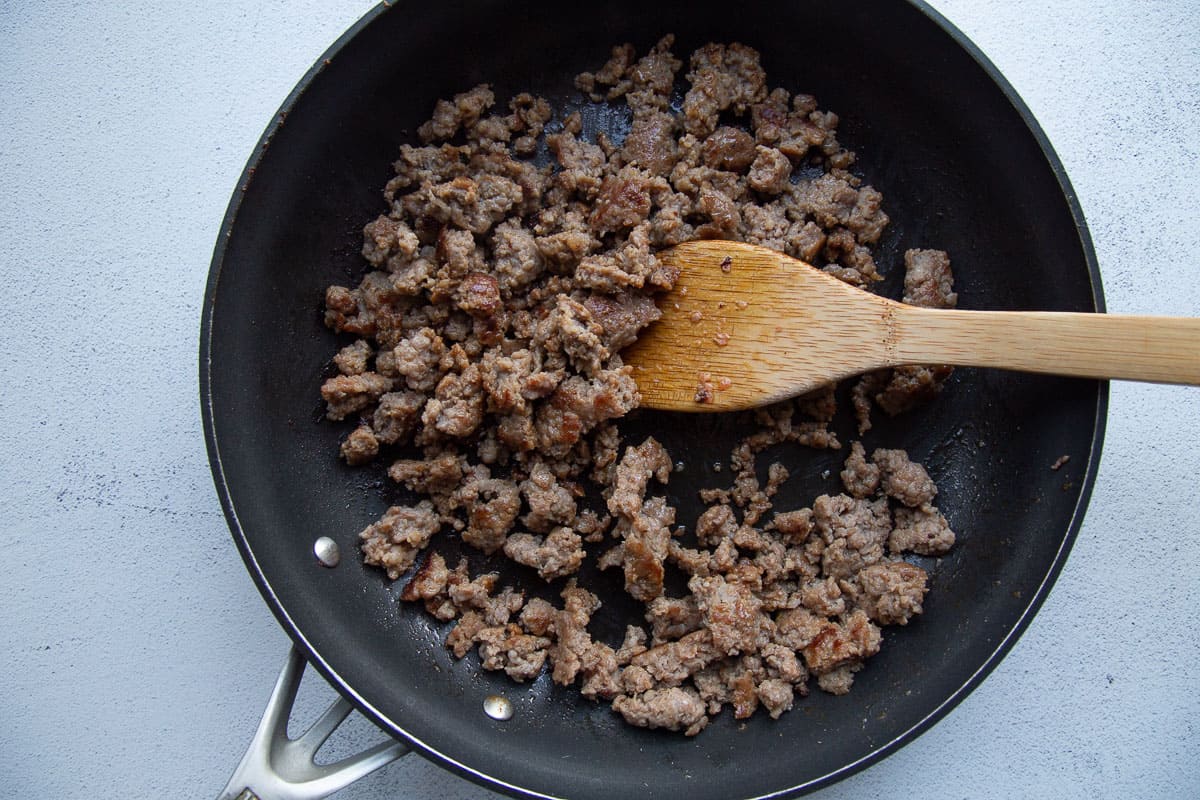 crumbled sausage in a skillet with a wooden spoon.