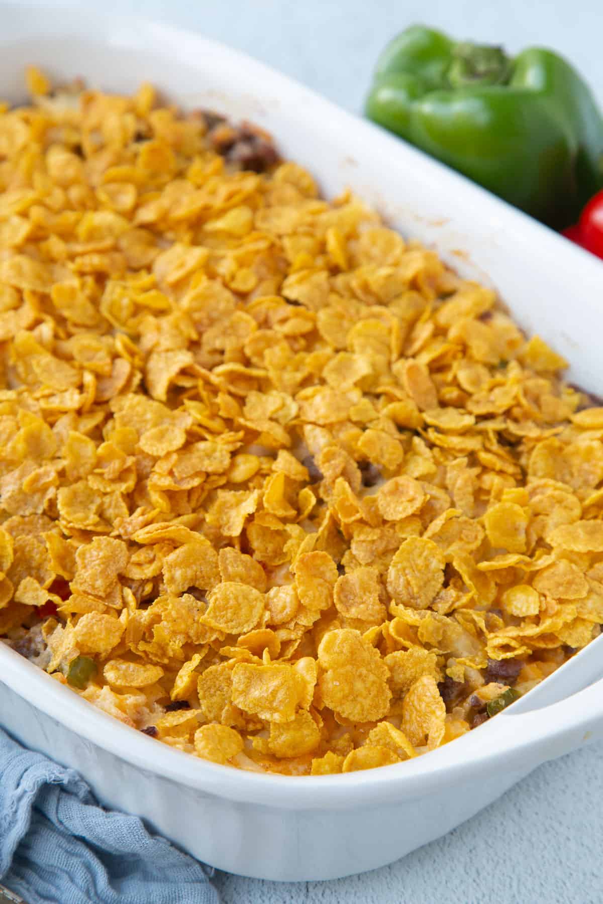 hash brown casserole topped with corn flakes in a white casserole dish.