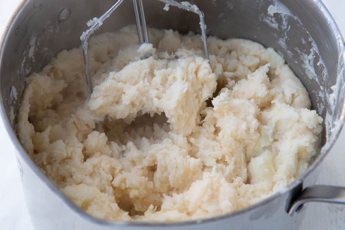 potato masher mashing potatoes in a large pot.