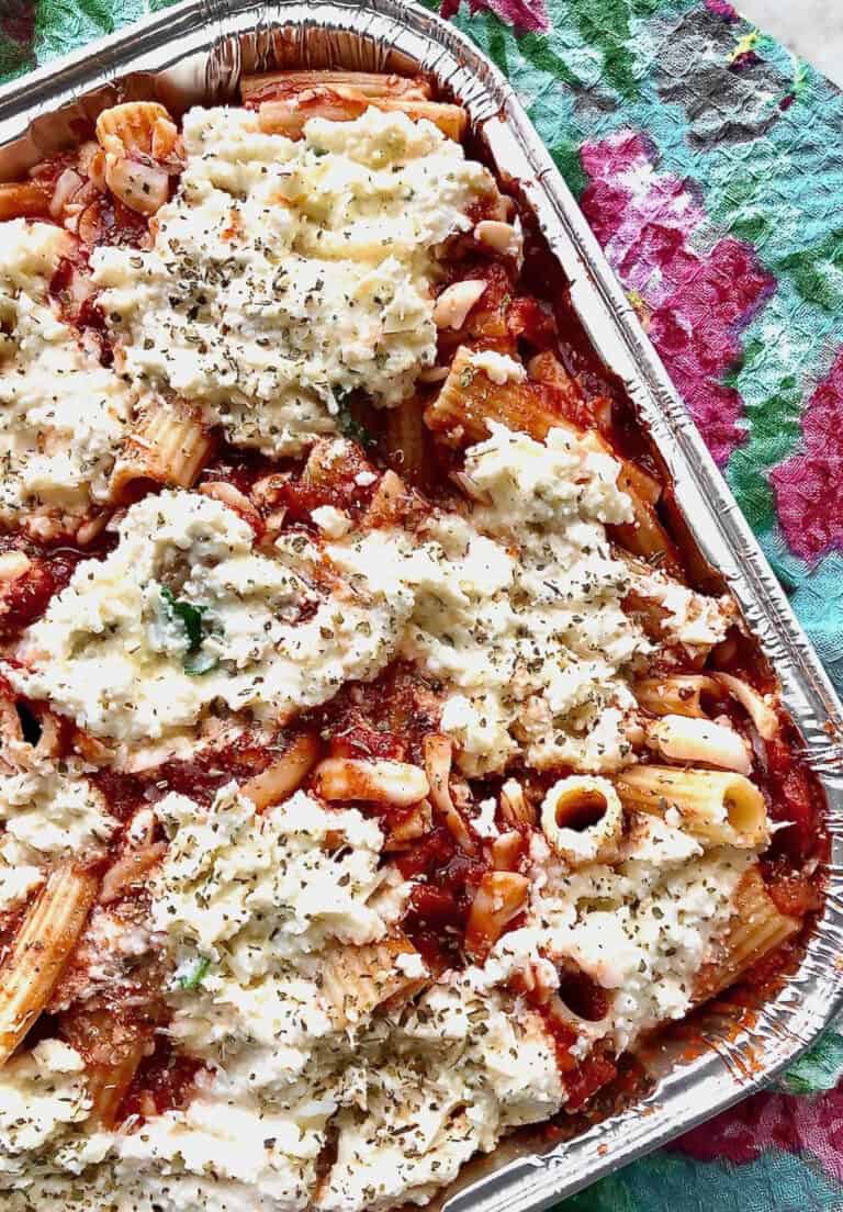 baked ziti in a foil casserole dish next to a floral napkin.