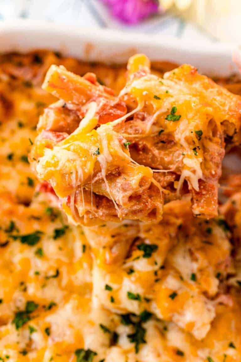 scoop of cheesy baked ziti being lifting out of a casserole dish.