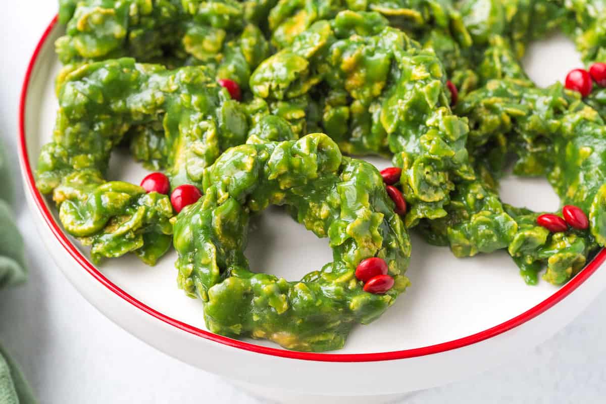 green corn flake wreaths with mini red M&Ms on a white cake stand with a red rim.