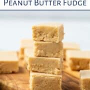 stack of peanut butter fudge along with more squares of fudge on a wooden tray.