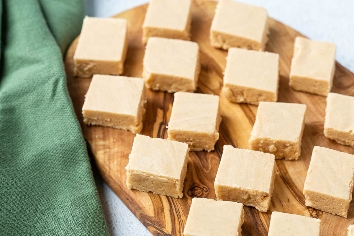 pieces of old fashioned peanut butter fudge lined up on an oblong wood serving board next to a green cloth napkin.