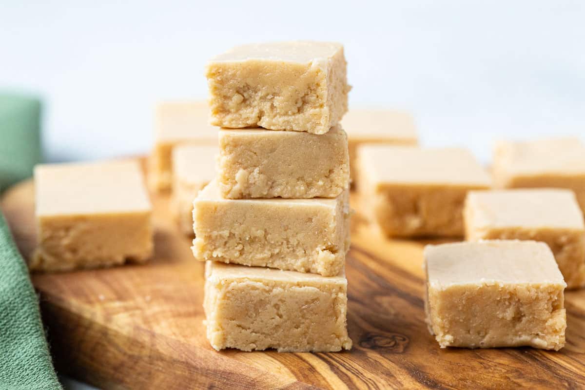 stack of peanut butter fudge along with more squares of fudge on a wooden tray.