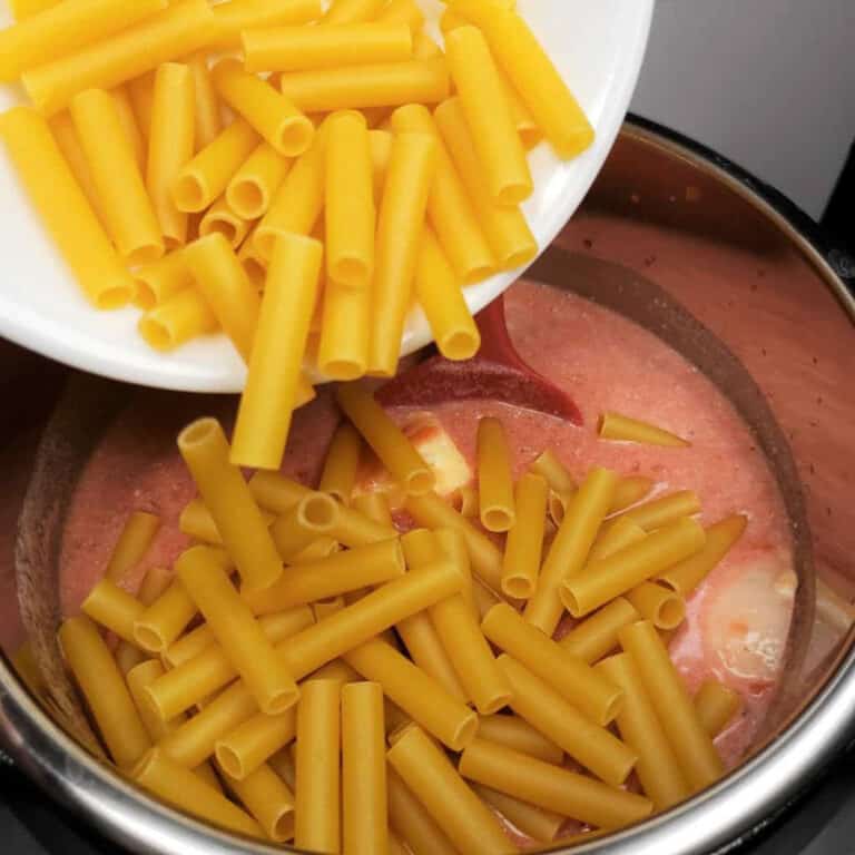 dried ziti being poured into an instant pot filled with a creamy tomato mixture.