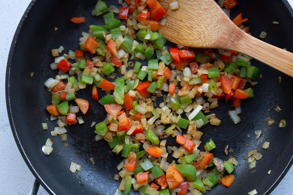 sautéed bell peppers and onions in a skillet with a wooden spoon.