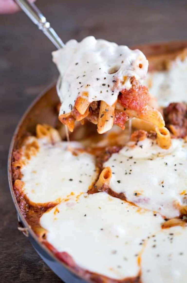 spoon lifting a spoonful of ziti covered with mozzarella cheese from a skillet.